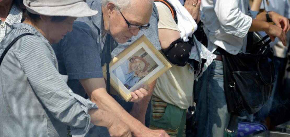 Bringing flowers and photos of their loved ones who have died from radiation poisoning, people pray on August 6, 2015, at a memorial in Hiroshima, Japan, that commemorates the victims of the atomic bombing of the city by the United States in 1945