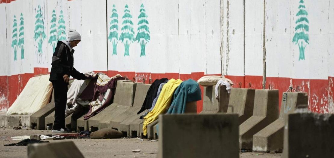 A displaced man puts his laundry on the sidewalk's concrete blocks at a parking lot in Beirut's waterfront area