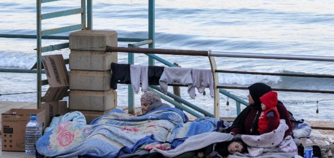 A displaced woman and her children sit near the sea at a makeshift encampment in Beirut